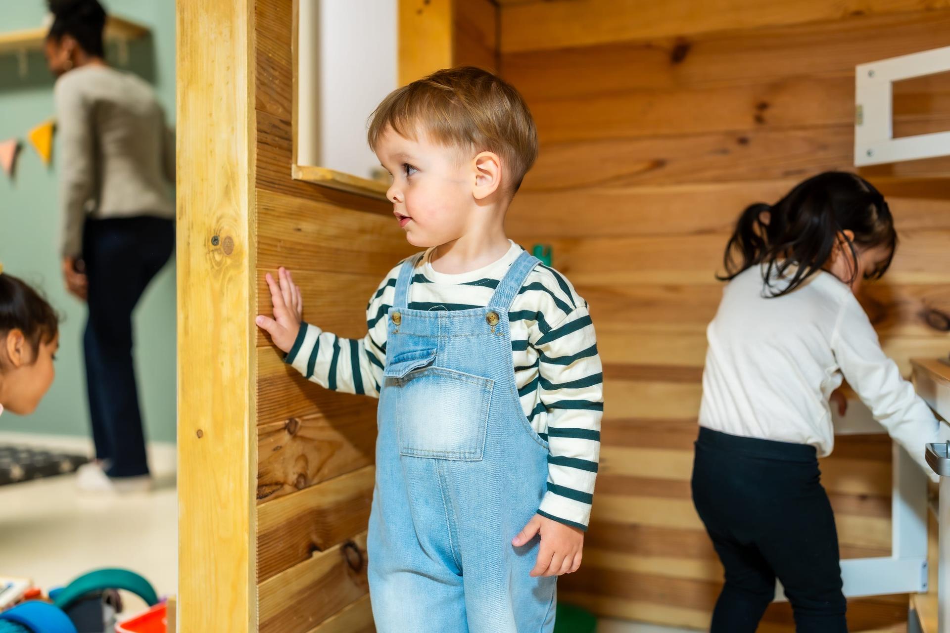 A toddler playing in a wooden playhouse at a daycare centre