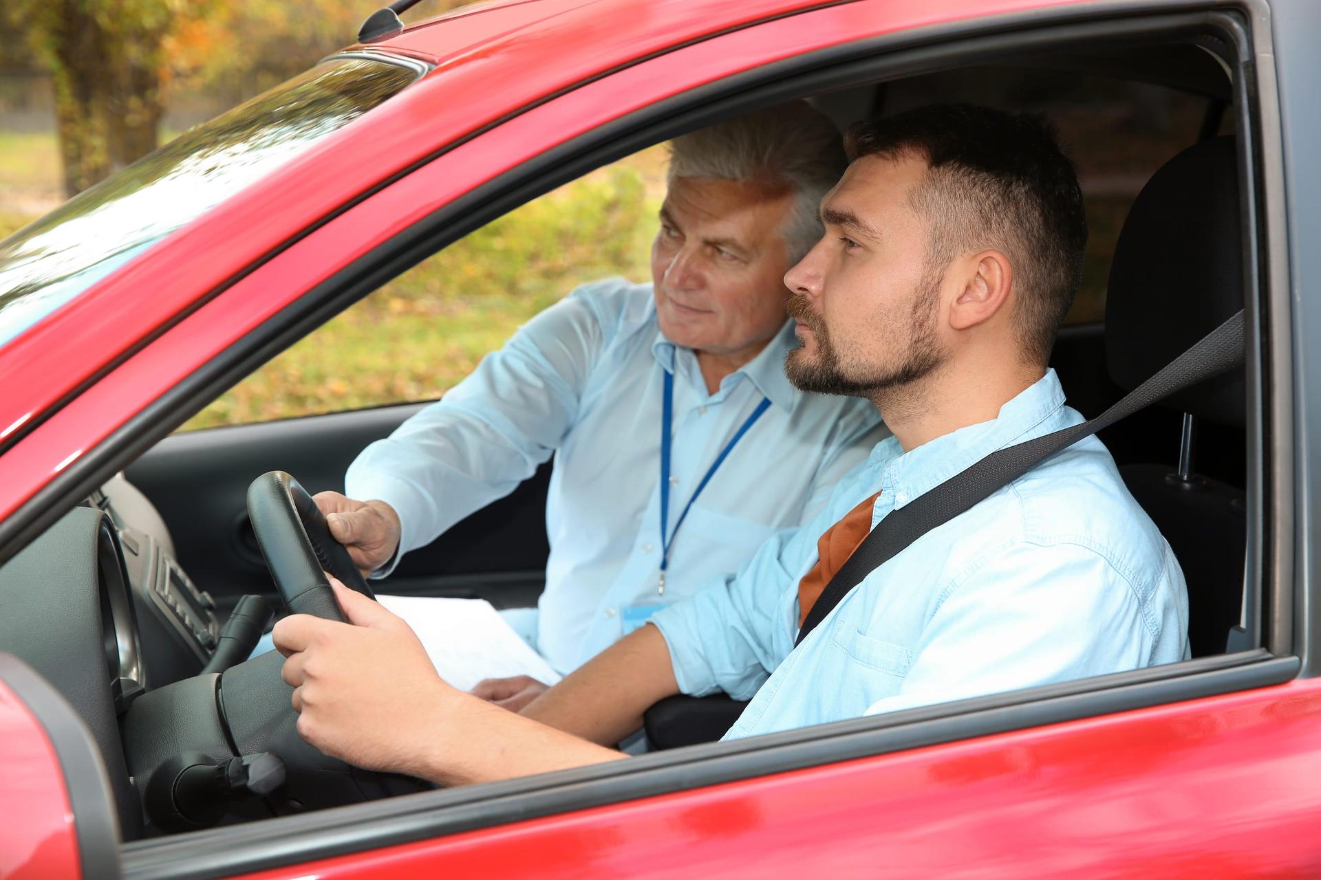 A learner driver at the wheel beside an instructor holding a clipboard