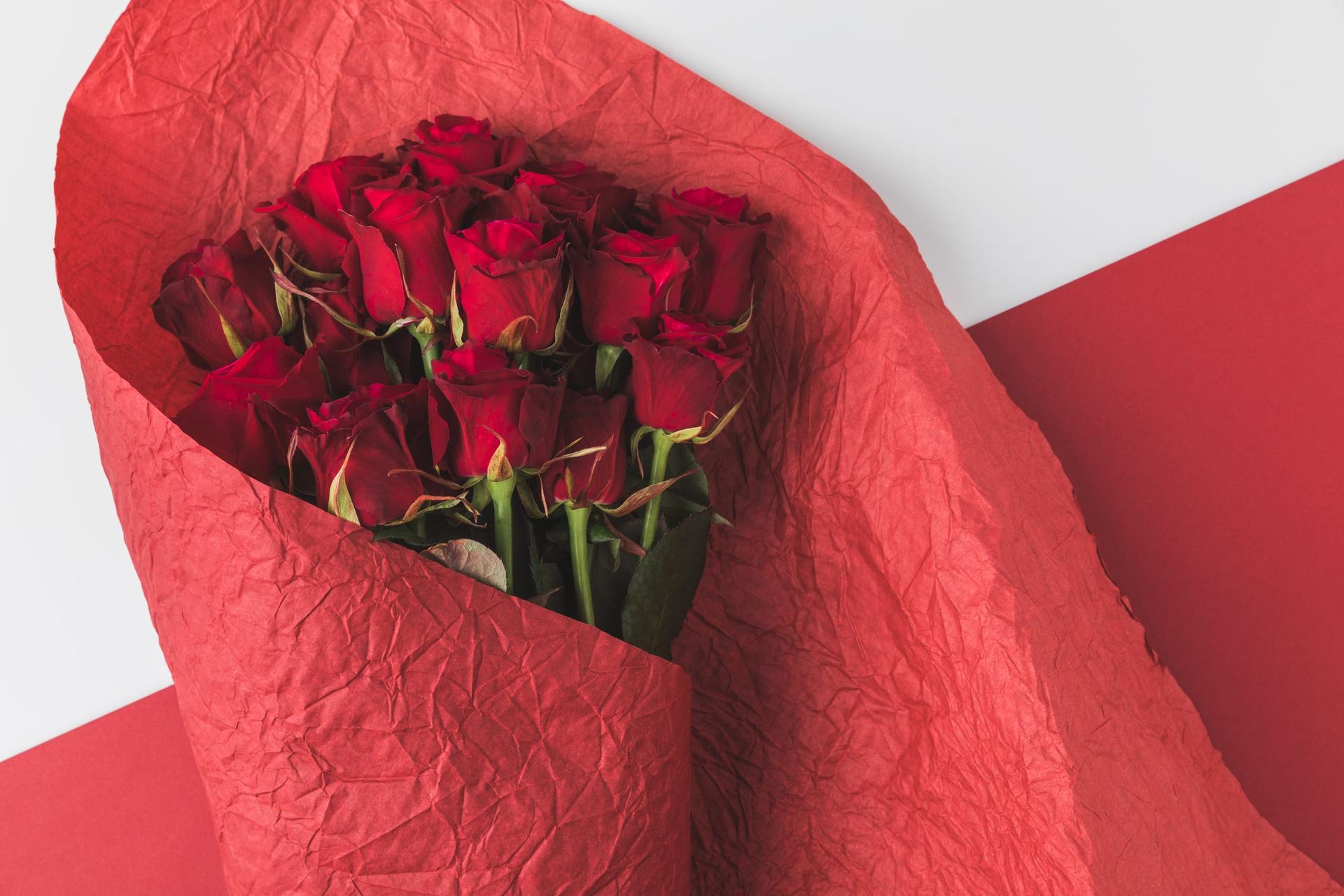 A bouquet of red roses wrapped in crumpled red paper, seen from above on a white and red background