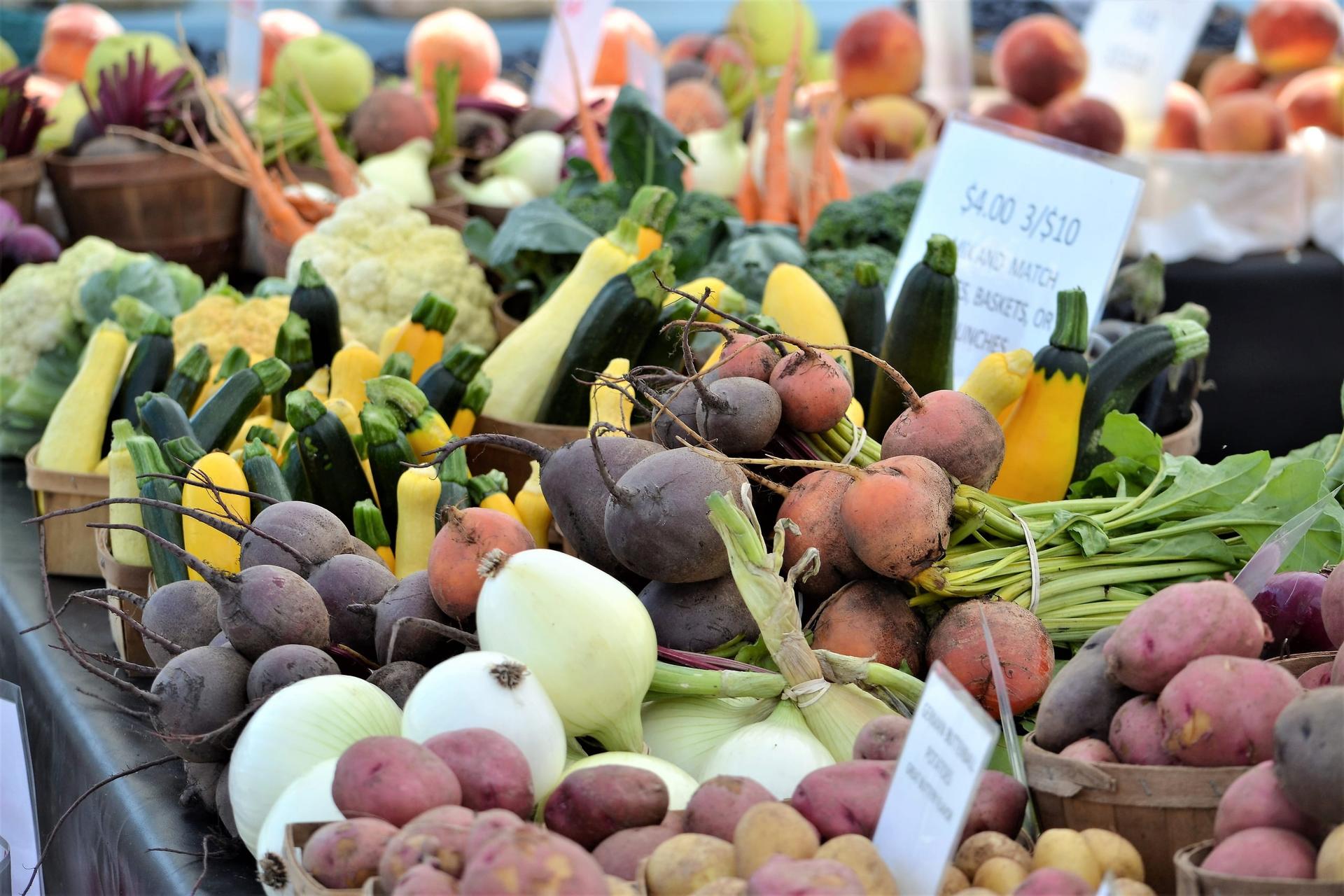 Baskets of beets, onions, potatoes and squash on a farmers' market table with handwritten price signs