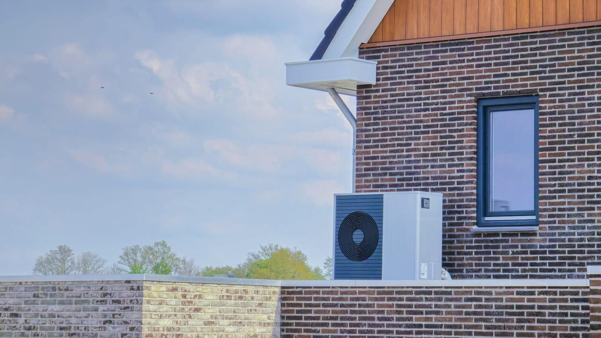 An air-source heat pump unit installed outdoors against the brick exterior wall of a modern home.