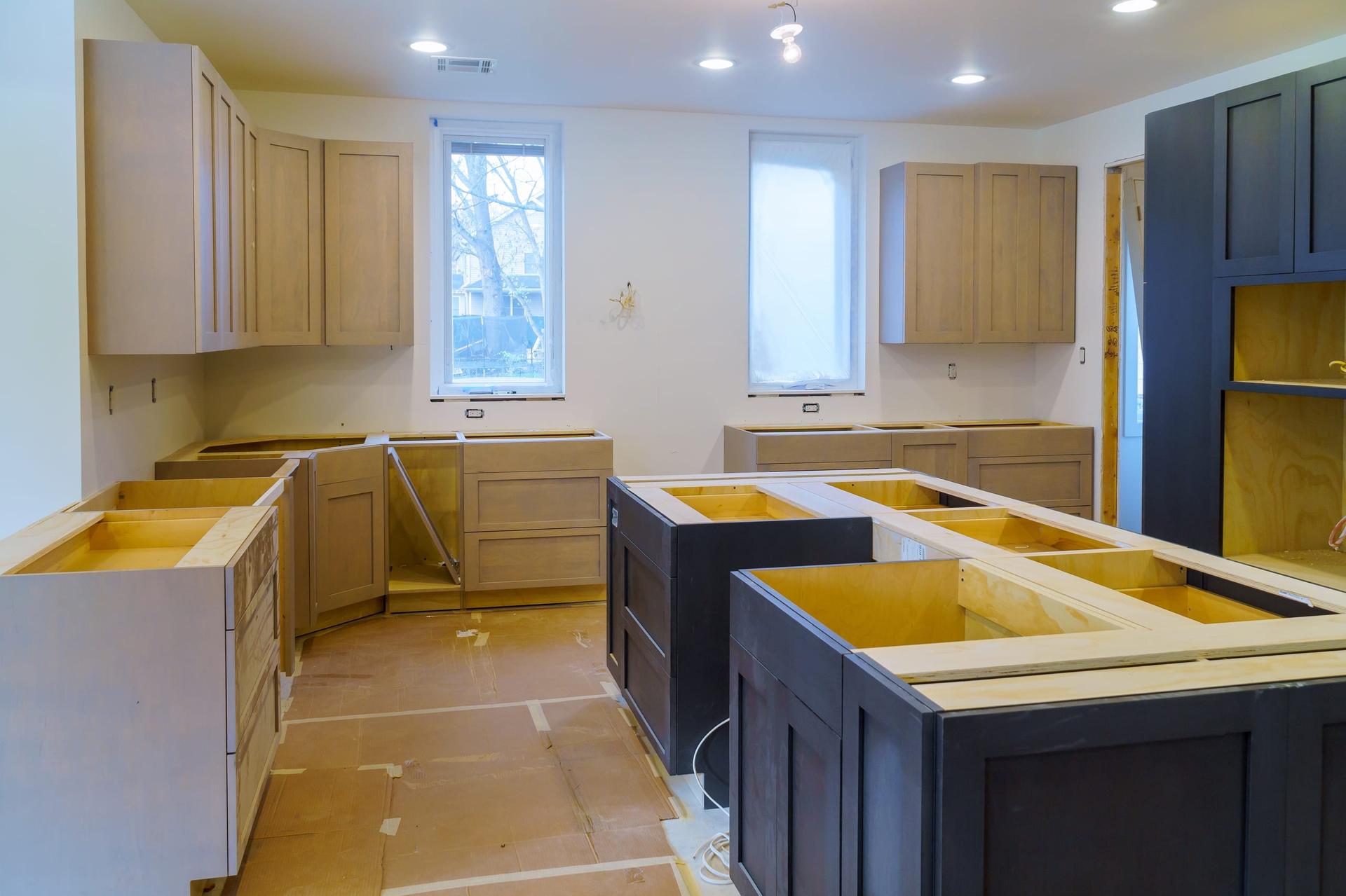 A kitchen mid-renovation, with unfinished wood cabinet boxes fitted along the walls and two dark island frames still waiting for countertops.