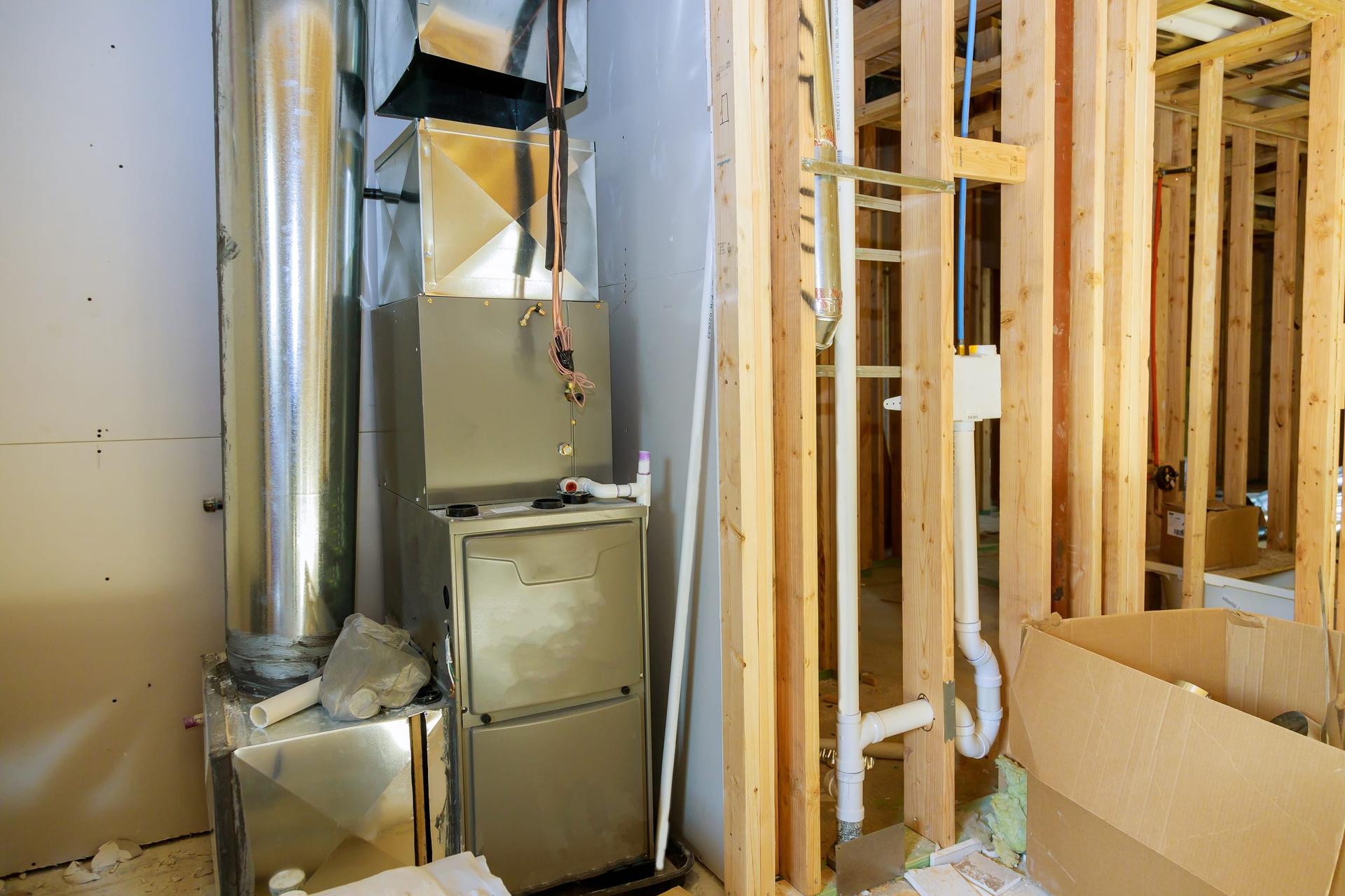 A new gas furnace with sheet-metal ductwork in an unfinished utility room beside wood framing