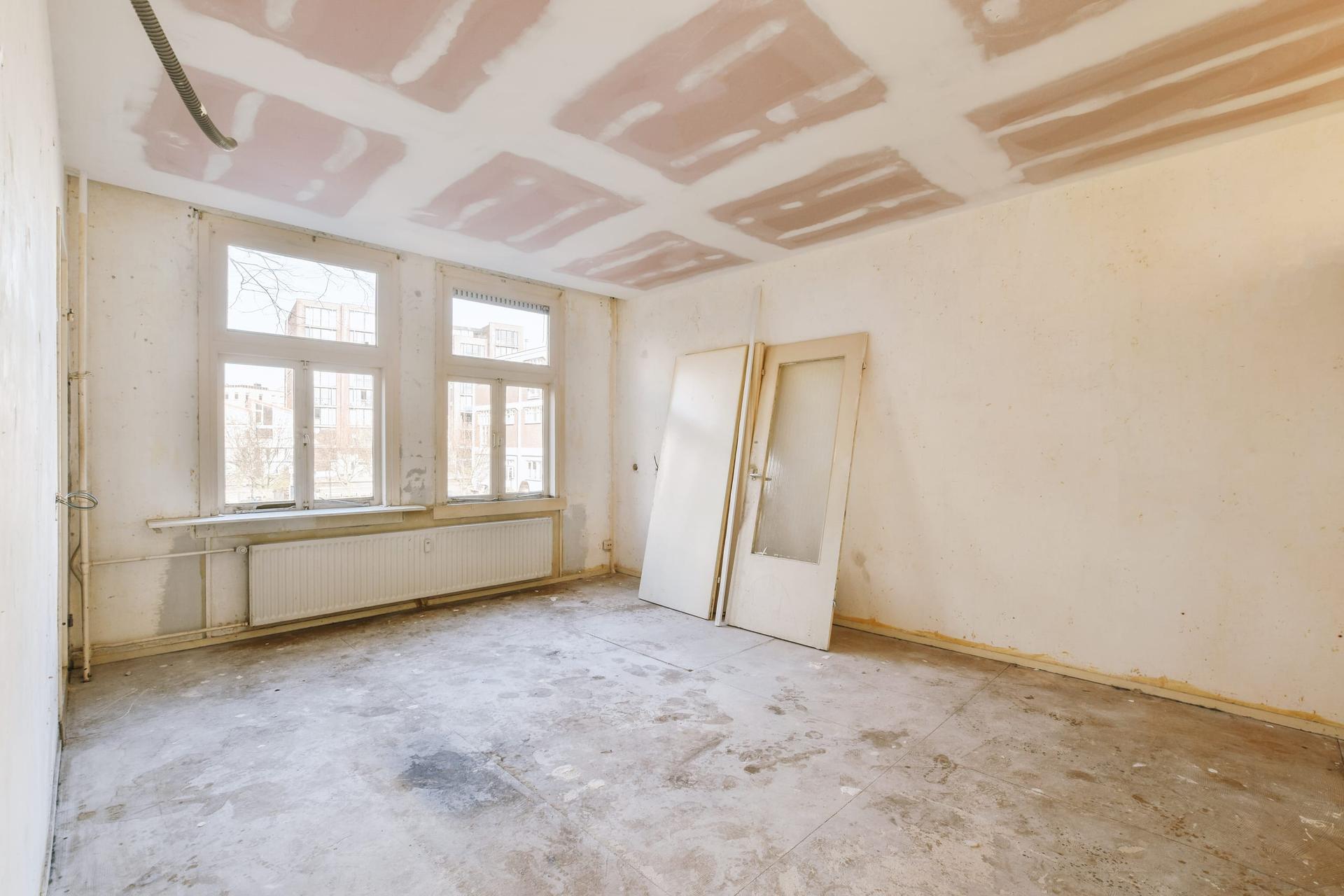 An empty apartment room with a window and a radiator