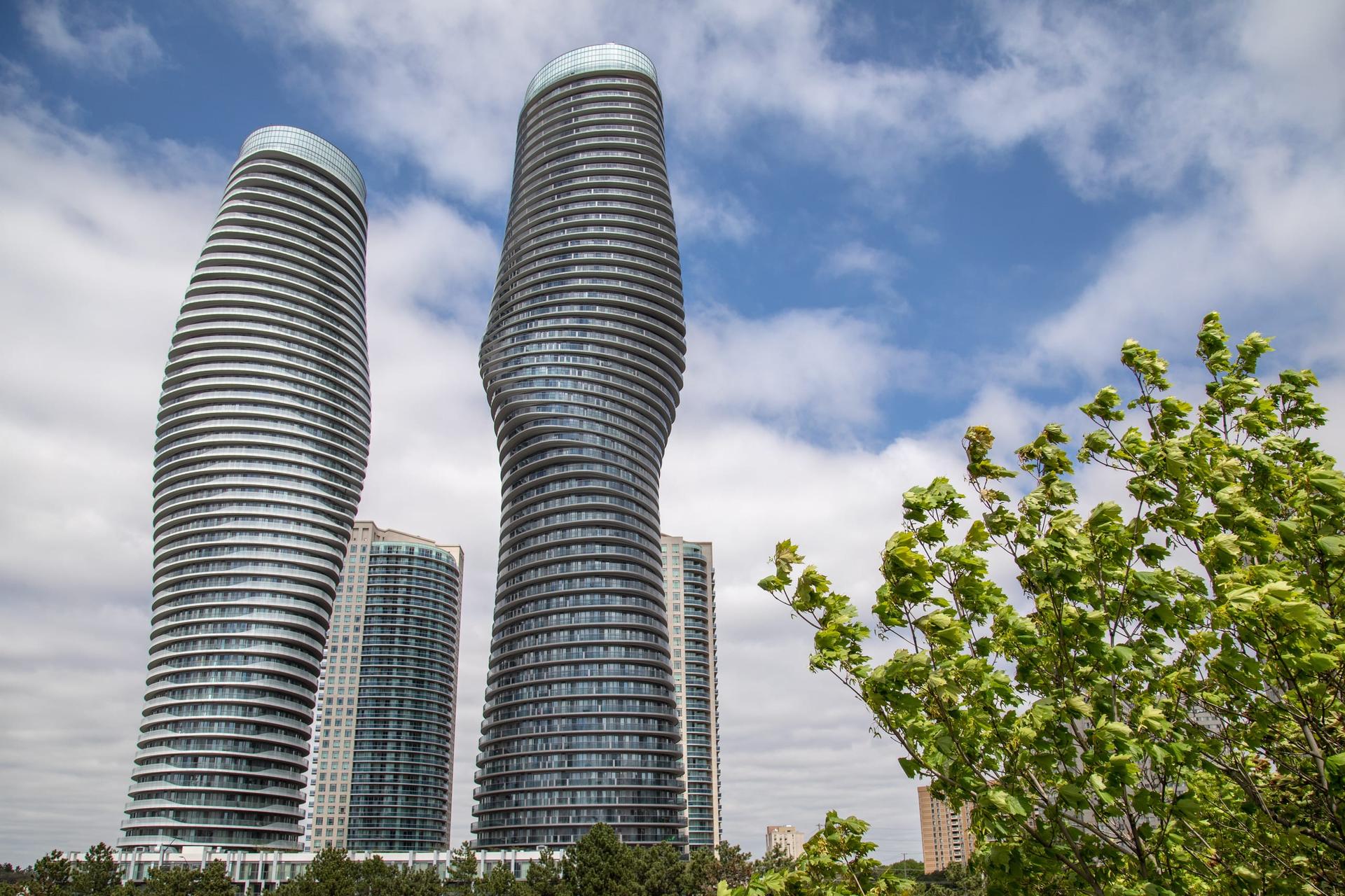 The two curved Absolute World towers rising above downtown Mississauga against a partly cloudy sky.