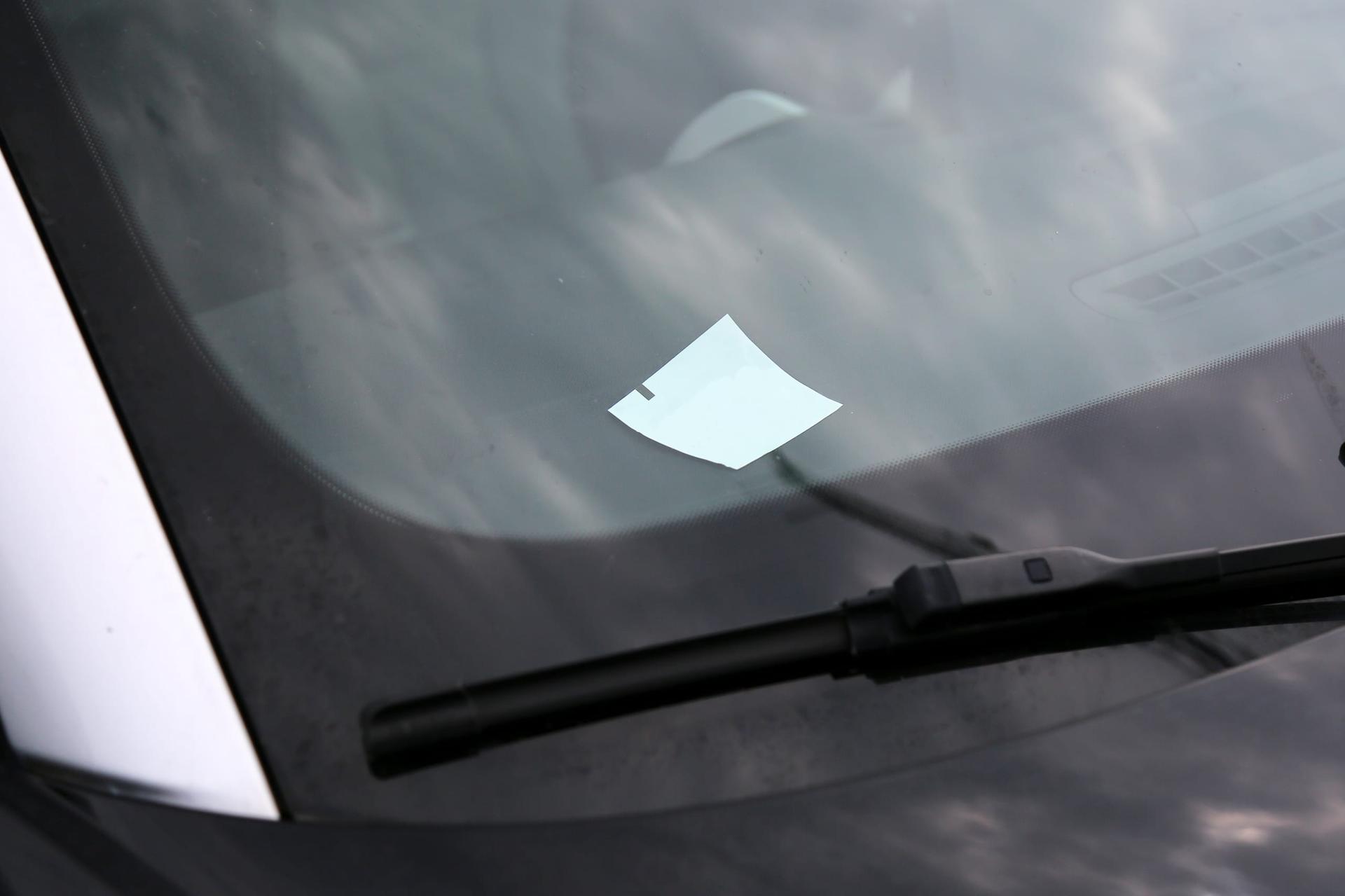 A slip of paper left under the windshield wiper of a grey car