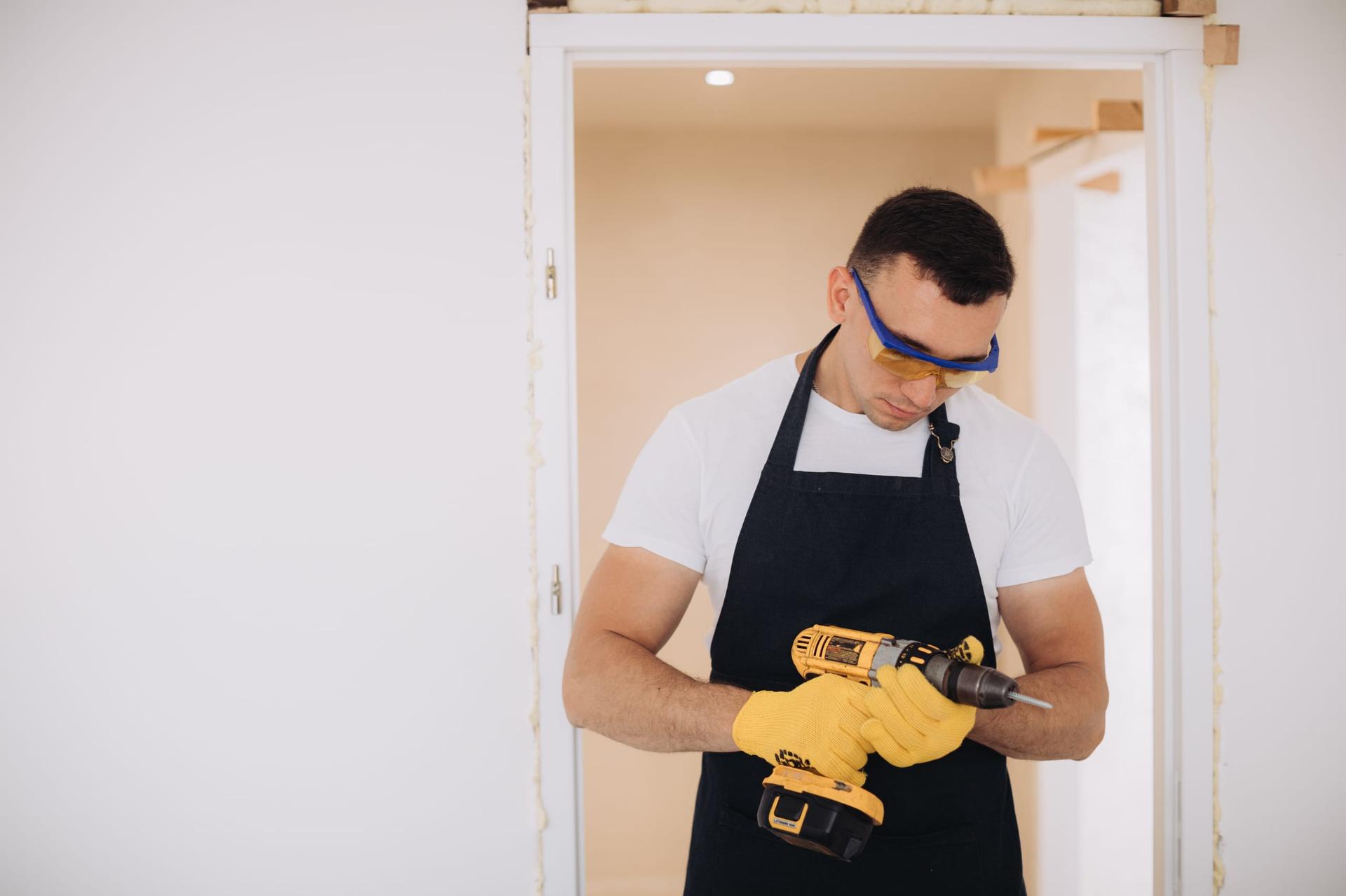 A maintenance worker uses a hand tool to adjust the hardware on an interior door.