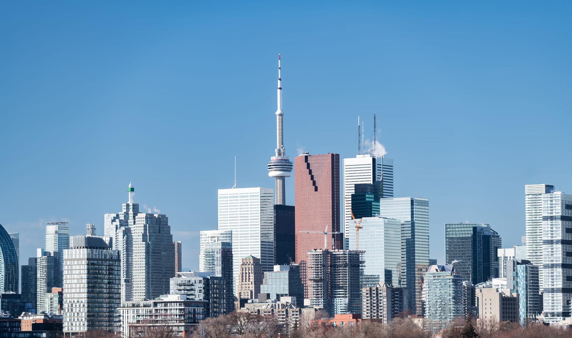 The downtown Toronto skyline with the CN Tower rising among office and condominium towers under a clear blue sky.