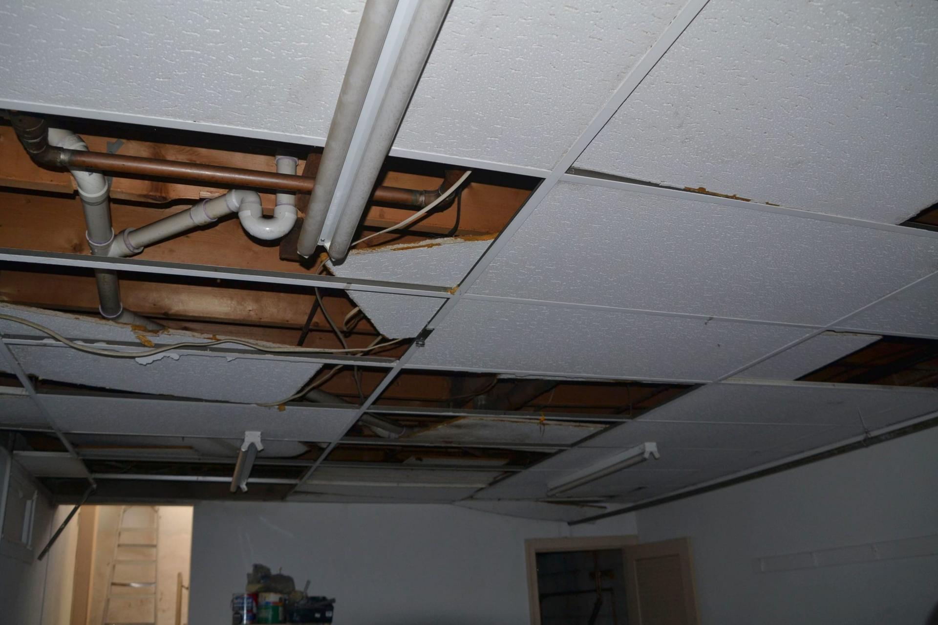A damaged drop ceiling with tiles removed, exposed pipes and water staining