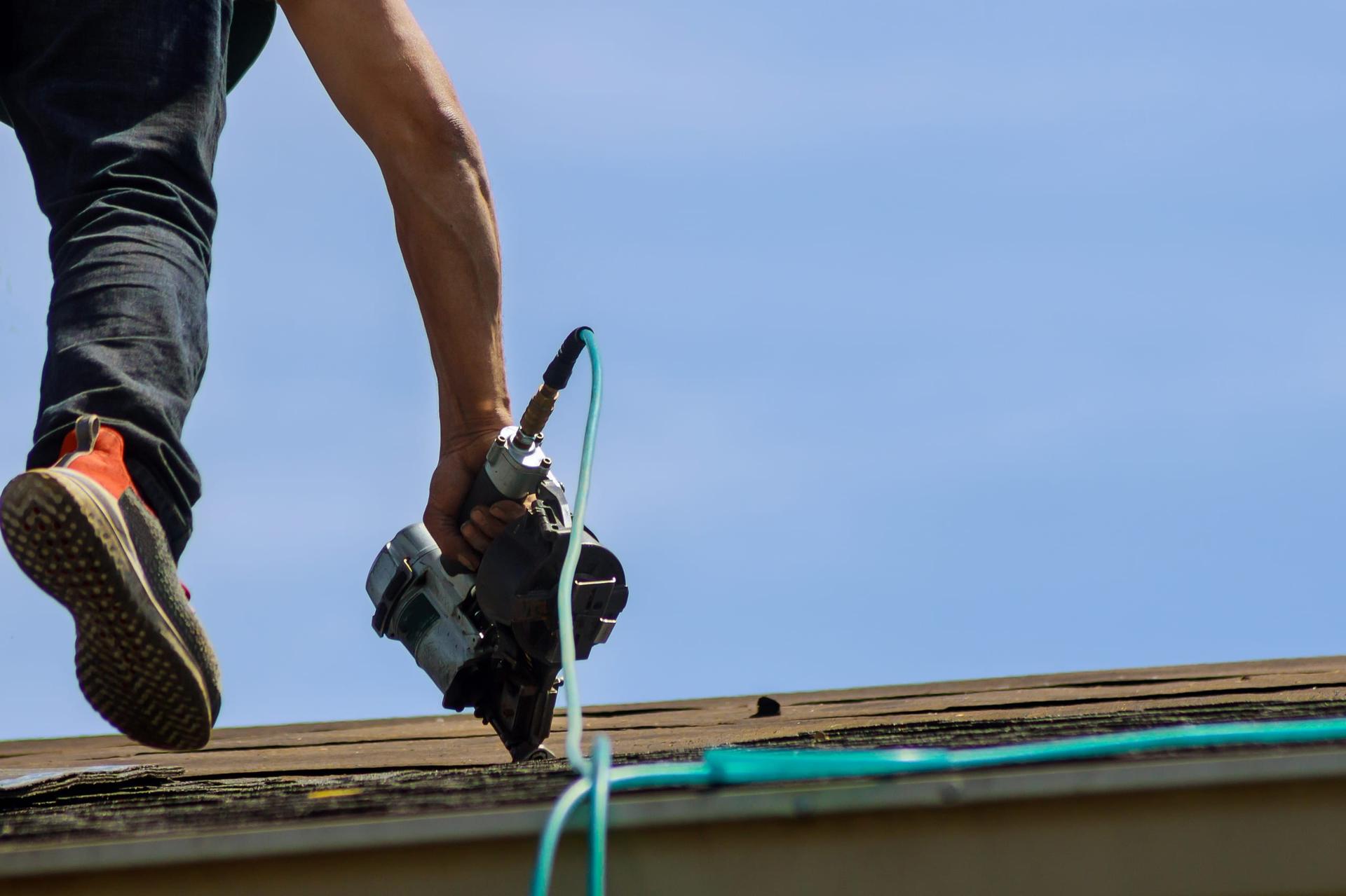 A roofer using a nail gun during a roof replacement