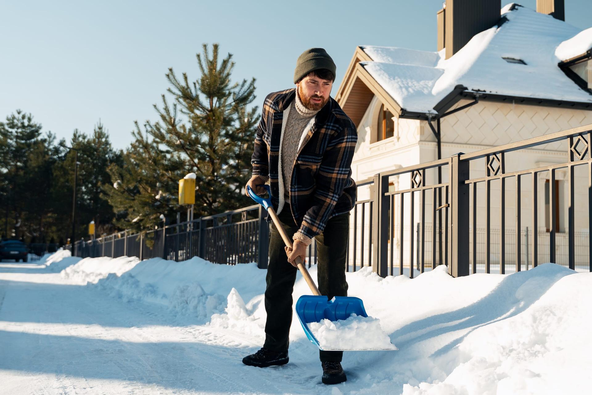 A resident shovelling snow from the walkway in front of a house